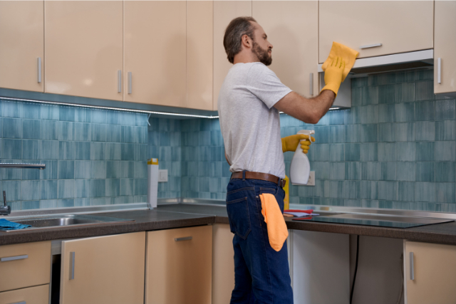 Young male worker cleaning kitchen furniture